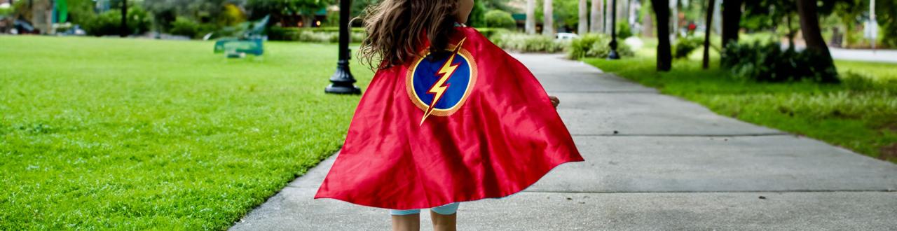 Girl running through the park with a cape